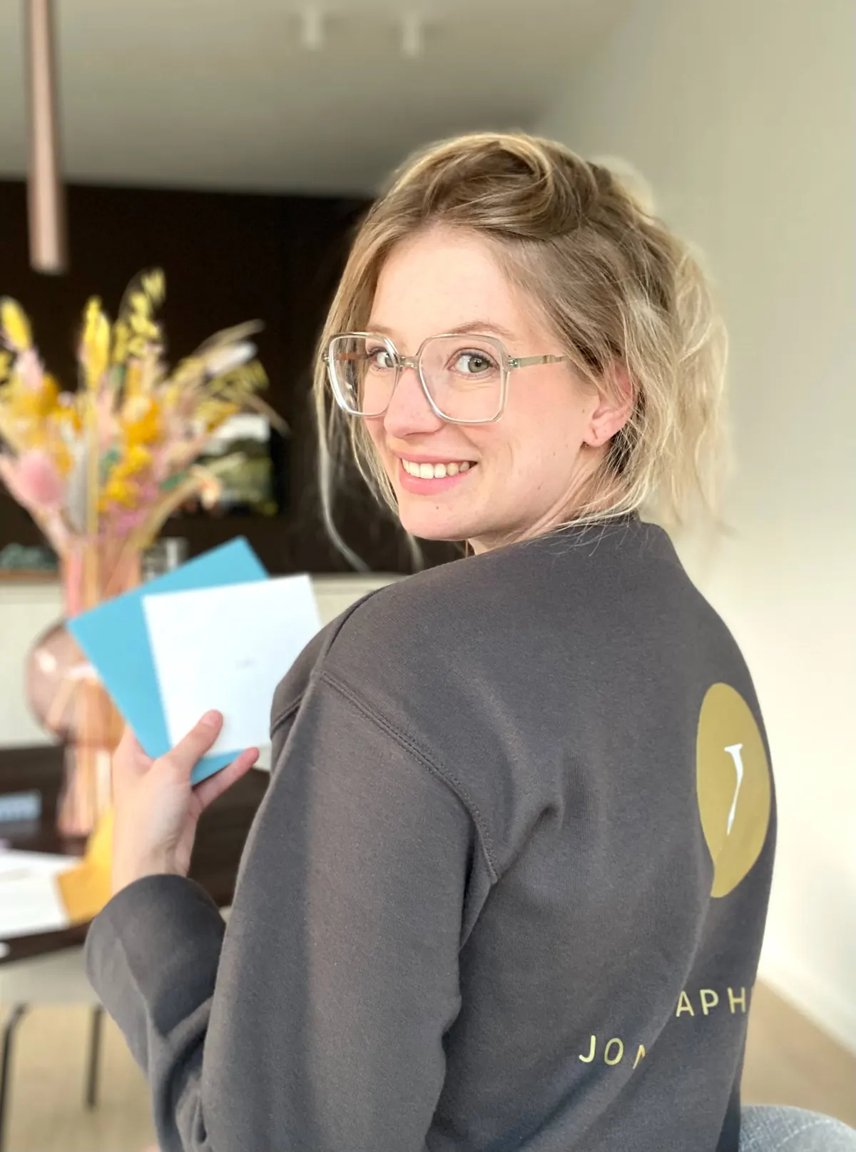 Jonie in een sweater met het logo van Jonie graphic design, met kaartjes en enveloppen in de hand