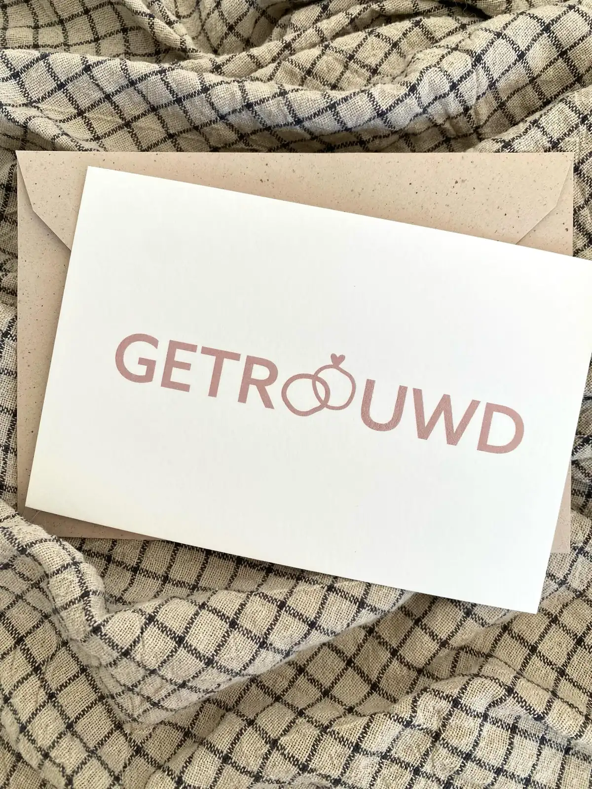Kaartje Getrouwd met twee verstrengelde trouwringen in het woord, in roze letters op witte kaart met kraftenveloppe