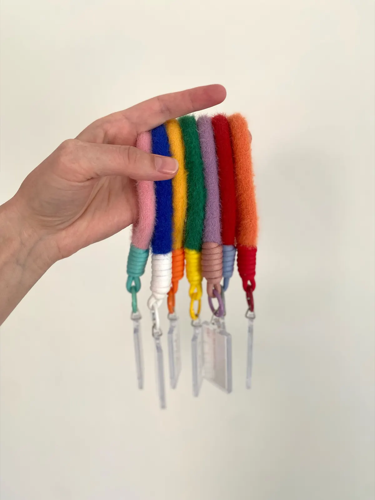 Zeven kleurrijke hangers met zachte vilten band en doorzichtig label, vastgehouden in één hand