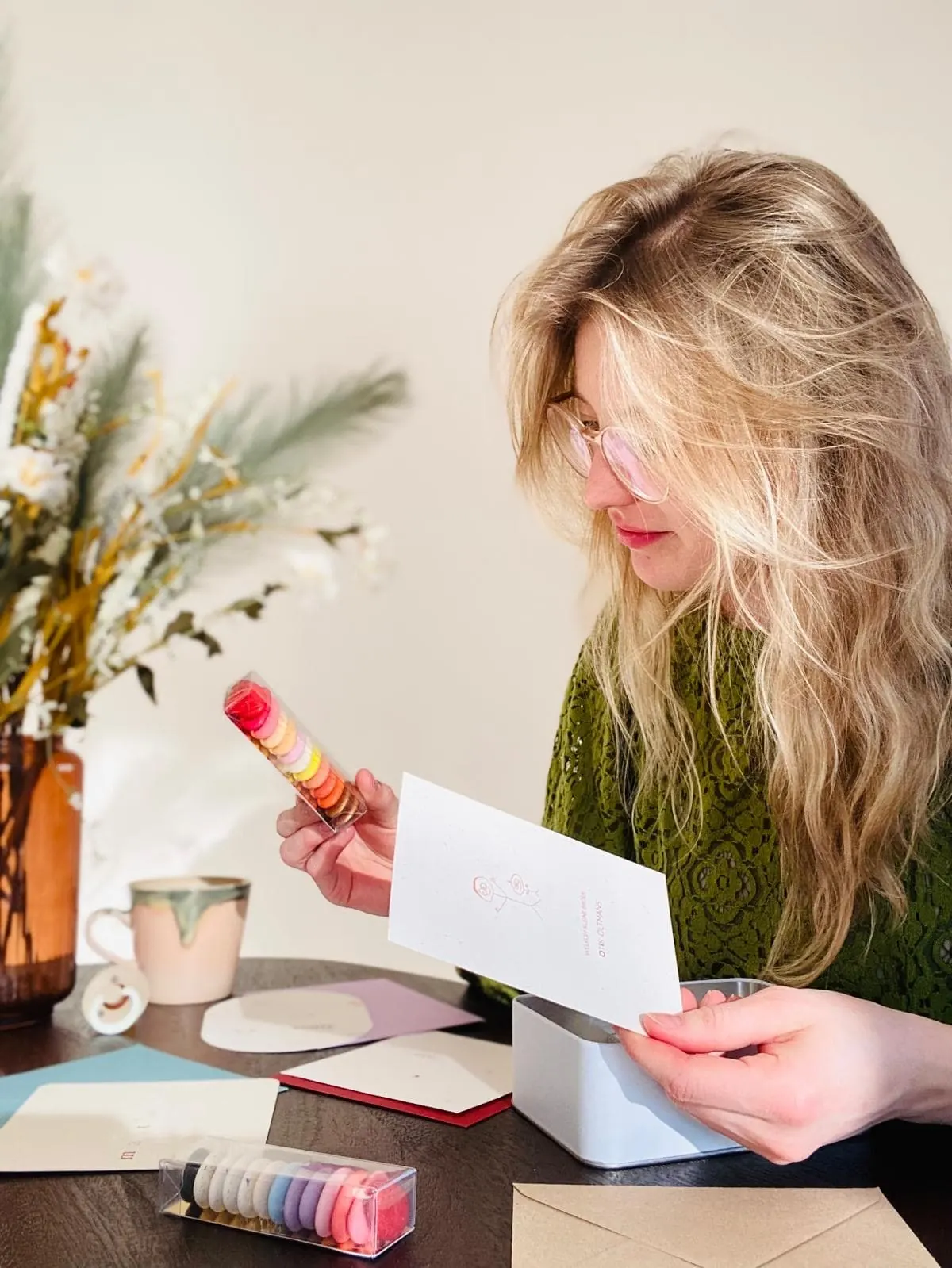 Jonie aan tafel met een geboortekaartje en doopsuiker in haar handen, omringd door kaartjes en gekleurde enveloppen